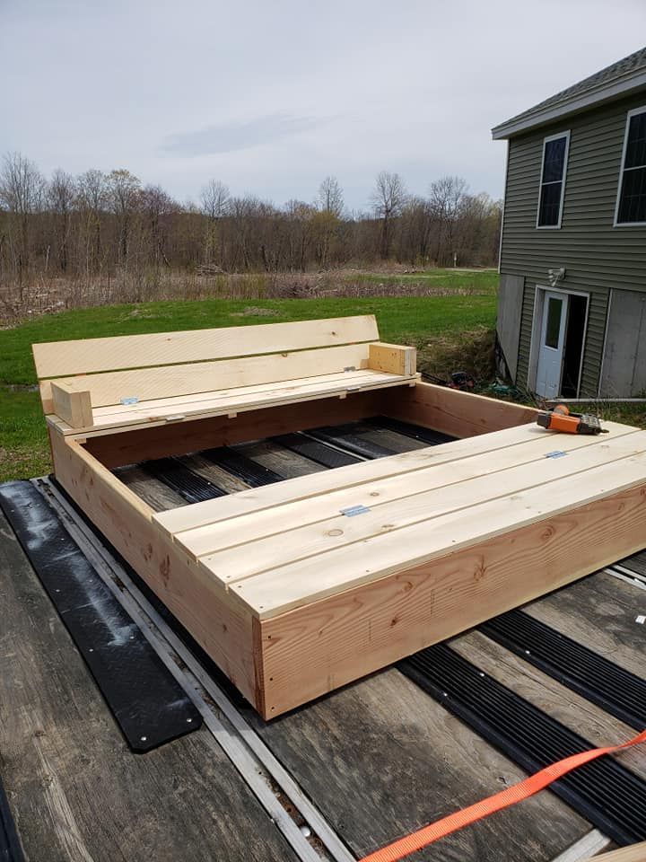 Partially built wooden deck frame beside a gray house on a trailer bed outdoors