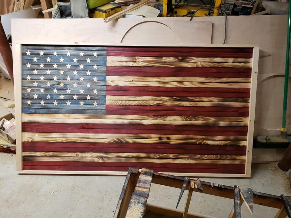 Weathered wooden American flag wall art in a workshop, with red, white, and blue paint.