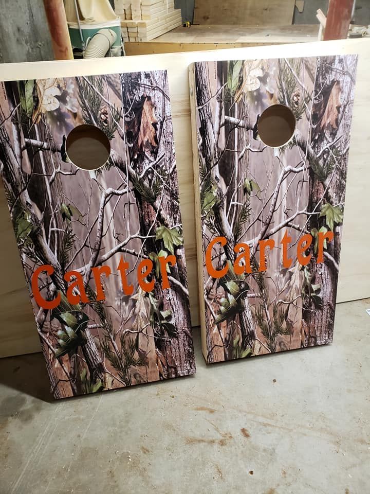 Two camouflage-patterned “Carter” cornhole boards leaning together on a concrete floor