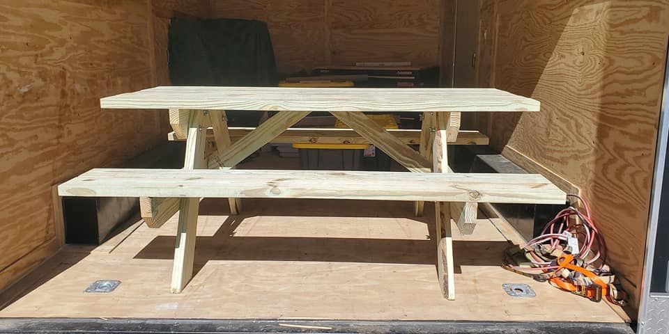 Wooden picnic table with benches inside a plywood-walled shed, with tools on the right side.