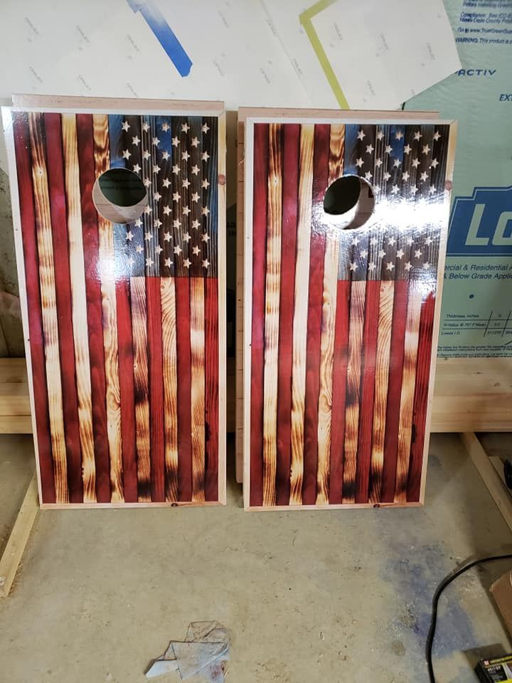 Two American flag cornhole boards standing side by side in a workshop or garage.