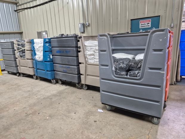 Row of wheeled laundry carts in a warehouse. Various colors, filled with linens.