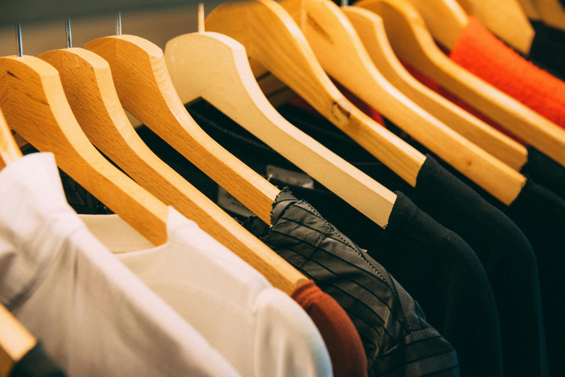 Clothes hanging on wooden hangers in a closet. White, black, and red clothing is visible.