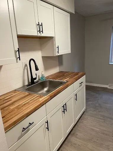 Kitchen sink area featuring white shaker cabinets, a light wood countertop, and a modern black faucet.