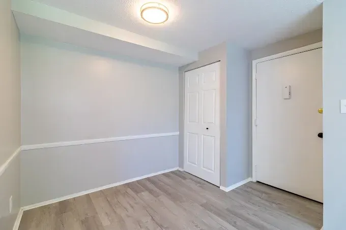 A small room with light grey walls, white trim, wood-look flooring, a white closet door, and a white entrance door.