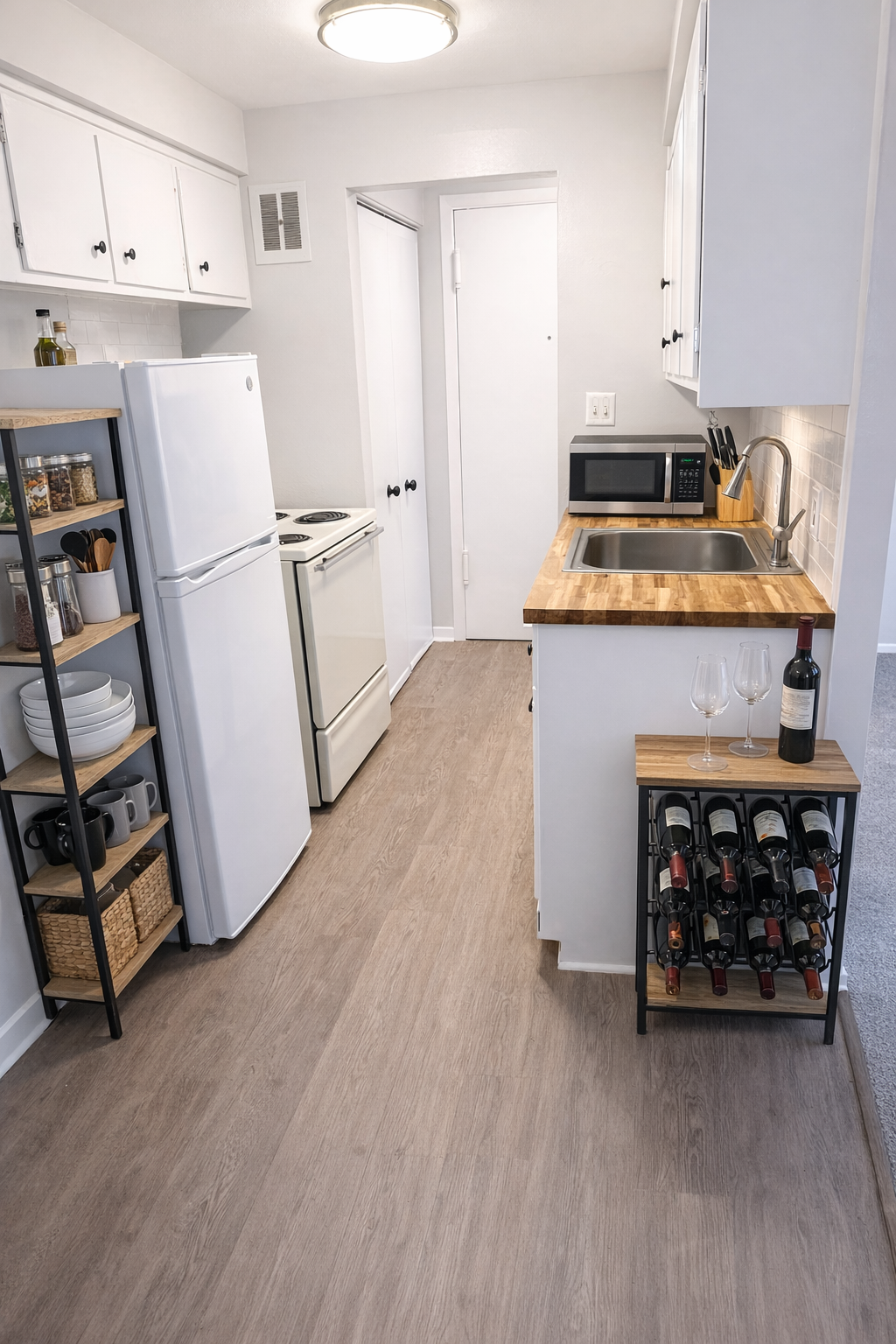 A galley-style apartment kitchen featuring white cabinets, wood-look flooring, a wine rack, and a wood-topped counter.