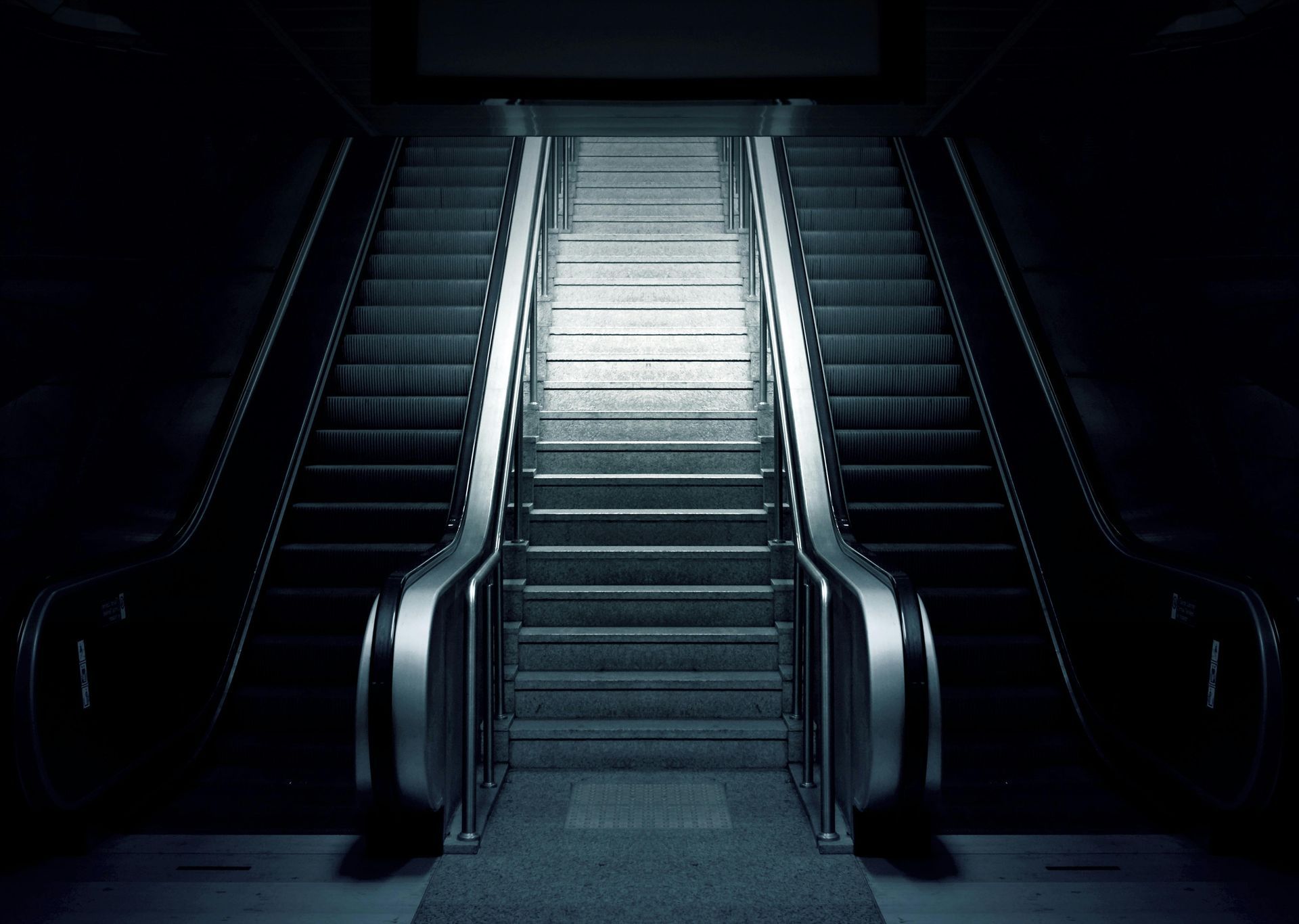Dark escalators with bright steps, descending into a dimly lit area.