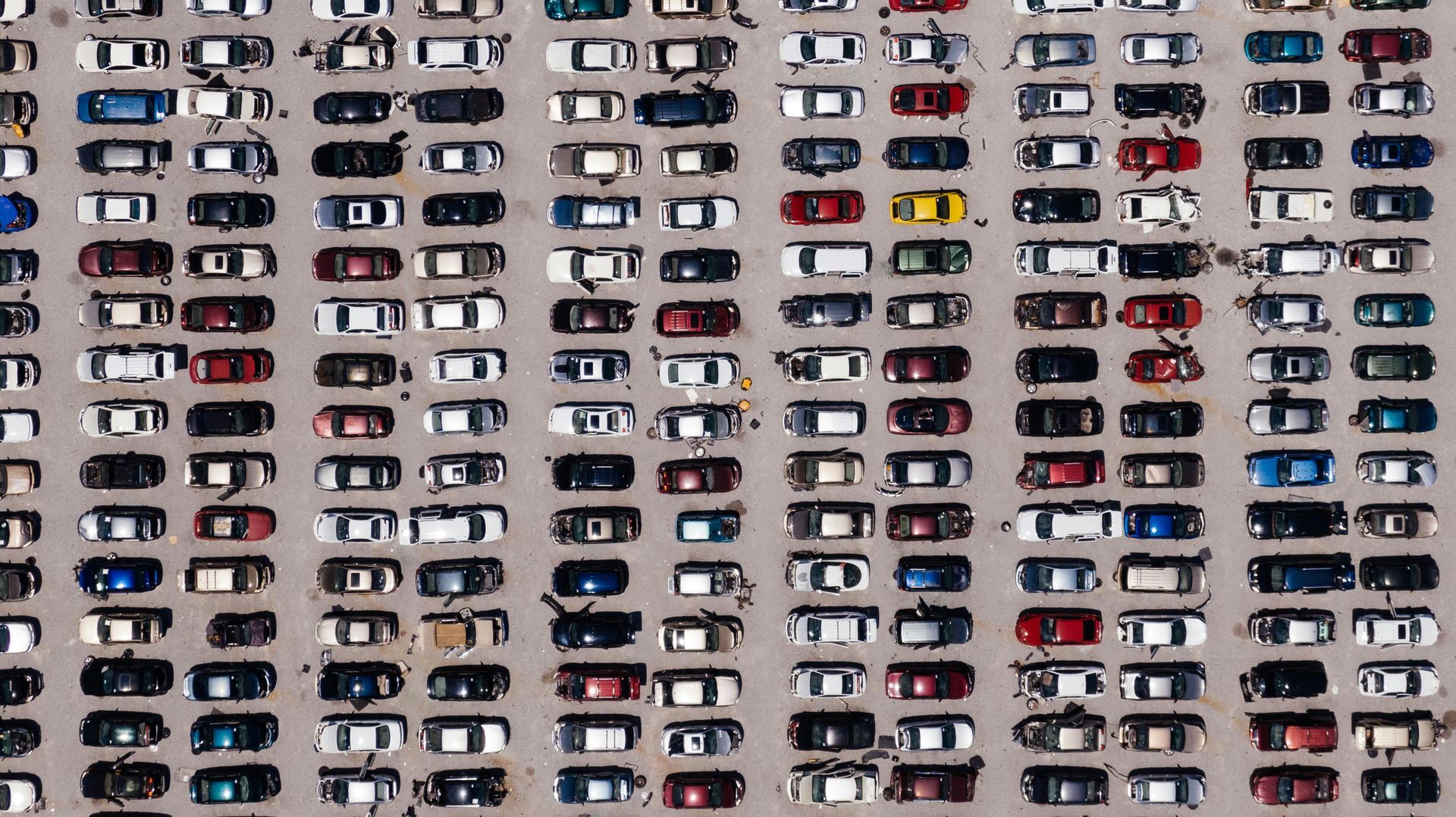 Overhead view of a large parking lot filled with many cars, mostly white, black, red, and blue.