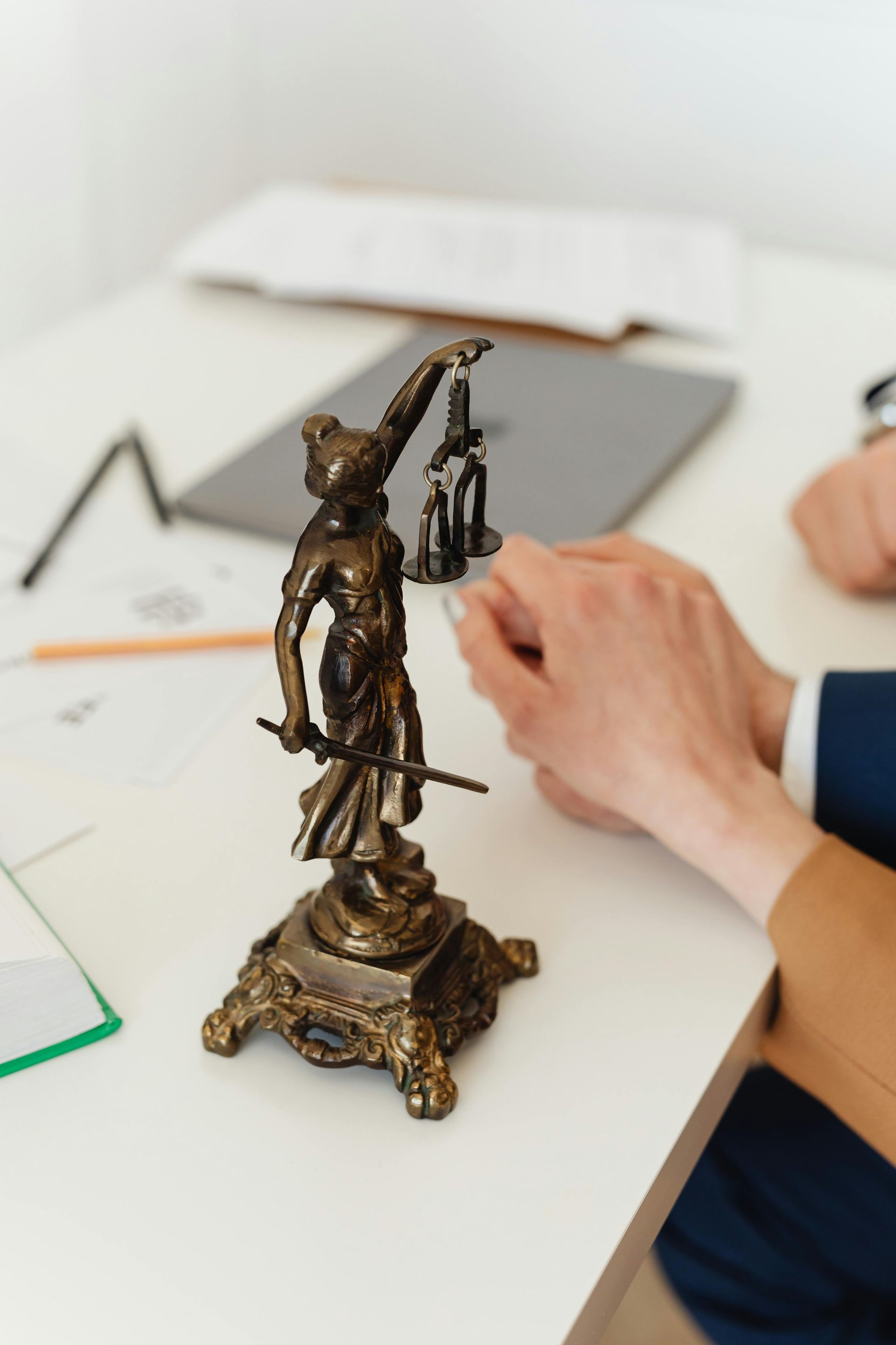 Statue of Lady Justice on desk with hands and documents.