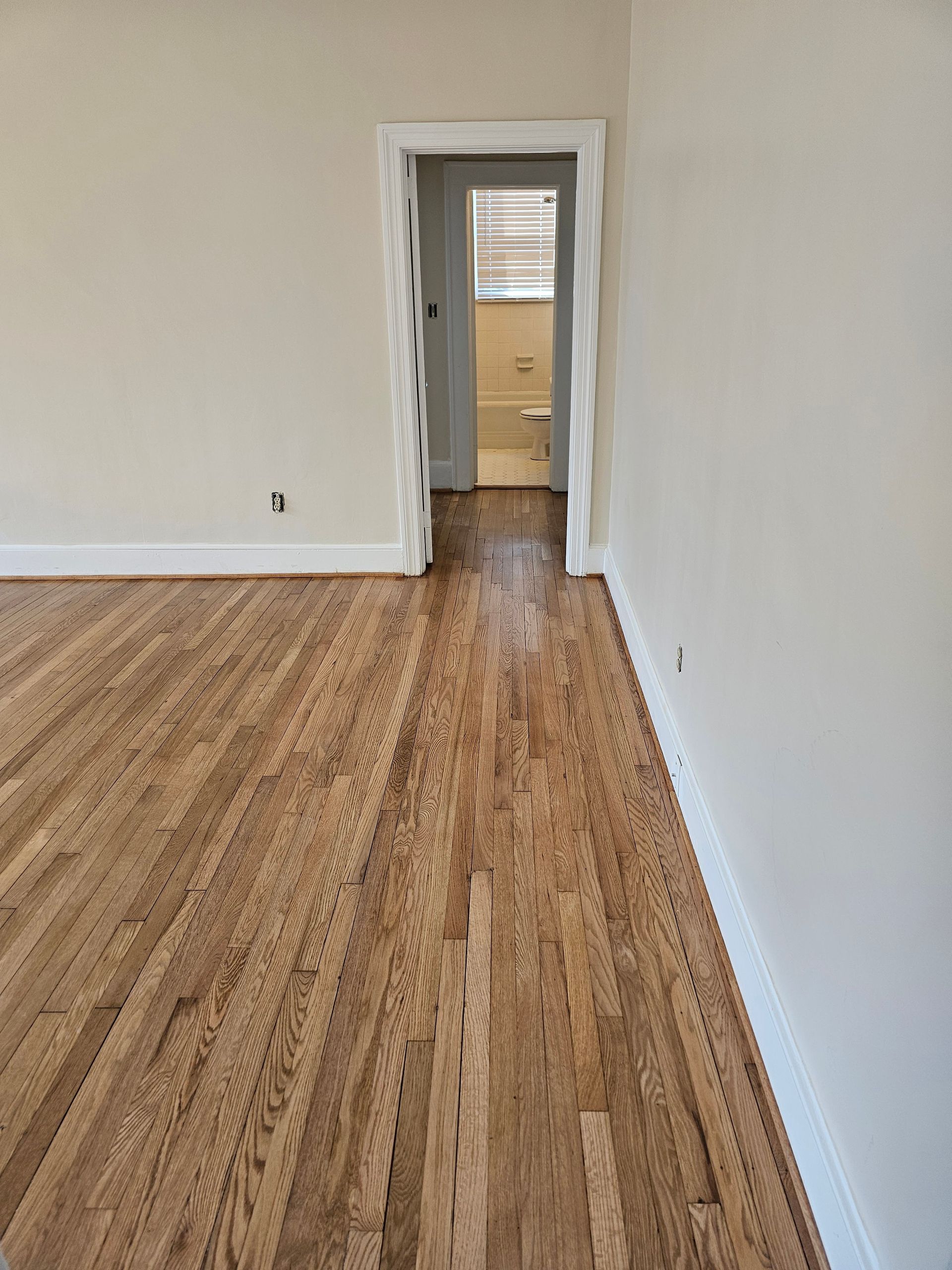 Hardwood floor leads to an open doorway into a light-filled room, white walls and trim.