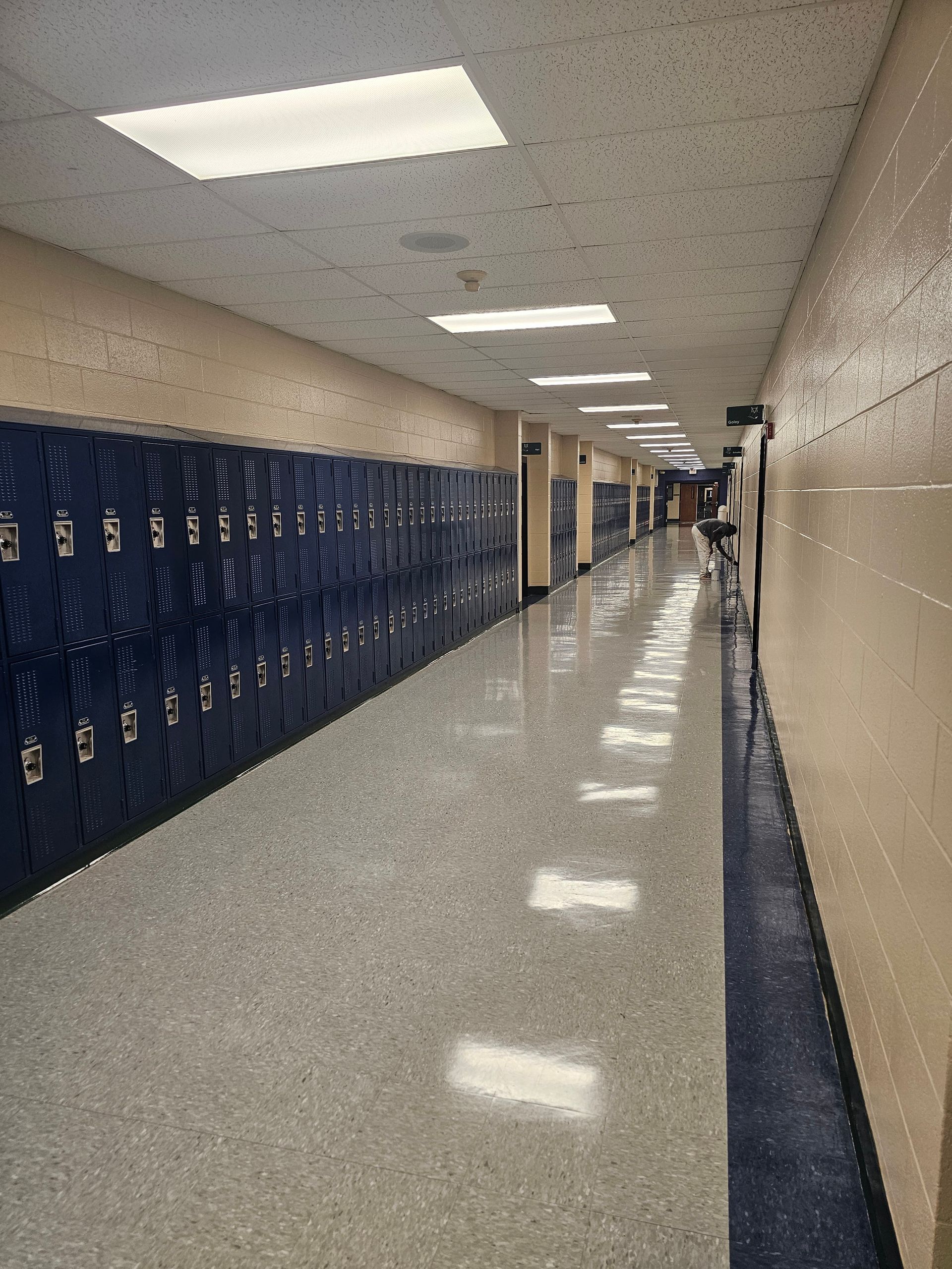School hallway with blue lockers, beige walls, and a reflective floor.