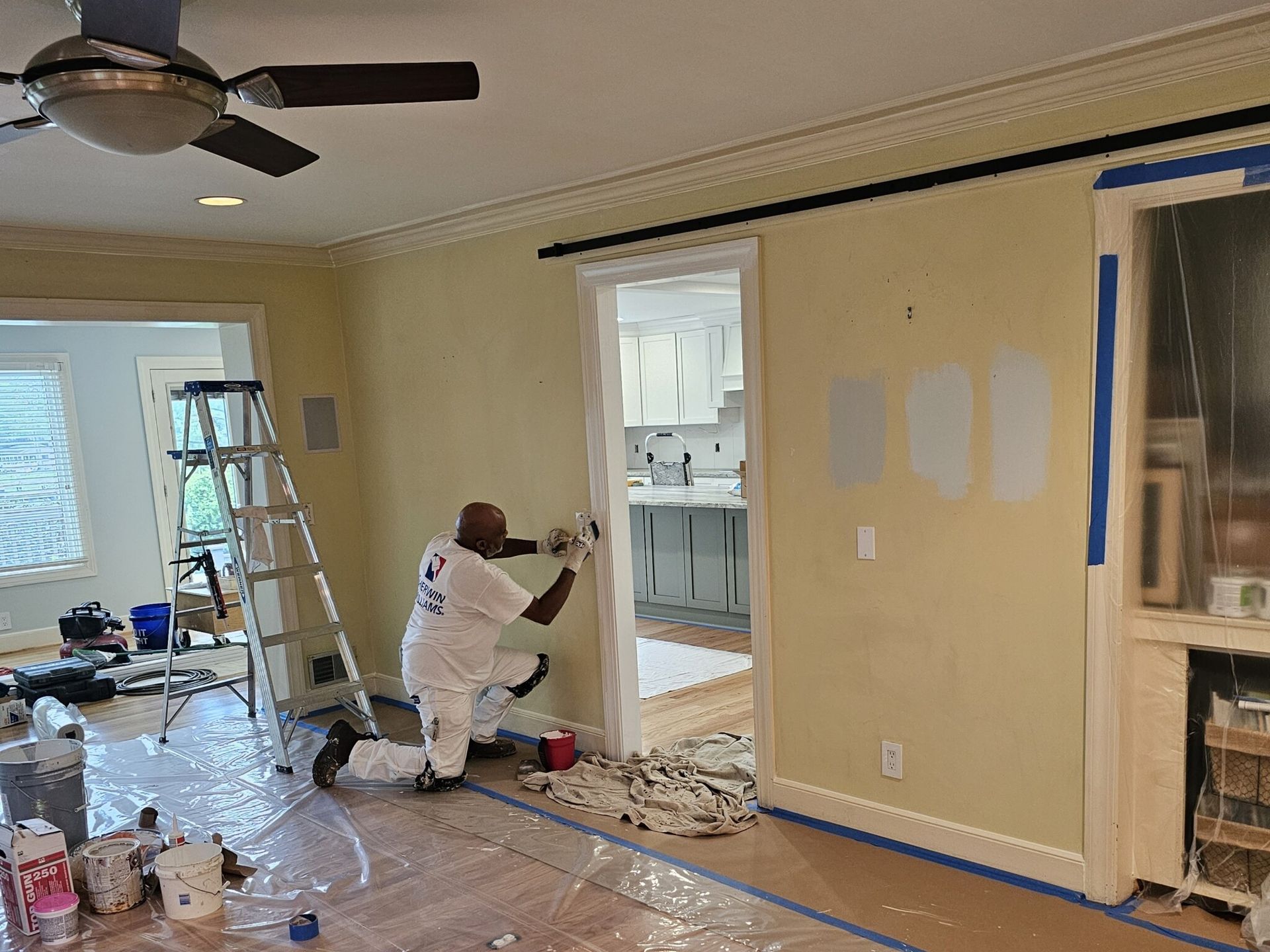 A person paints a doorway in a room with pale yellow walls. Tools and paint cans are on the floor.