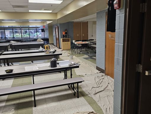 School cafeteria under renovation; tables, tools, and paint cloths on the floor.