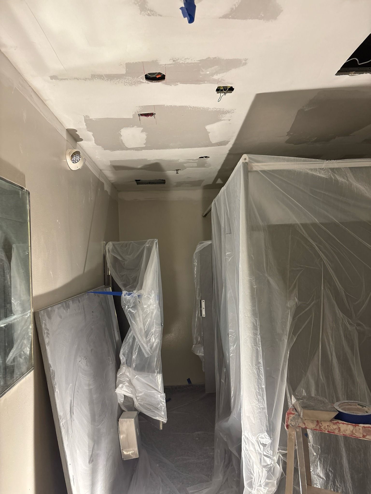 Narrow hallway under construction, covered surfaces, exposed ceiling with holes.