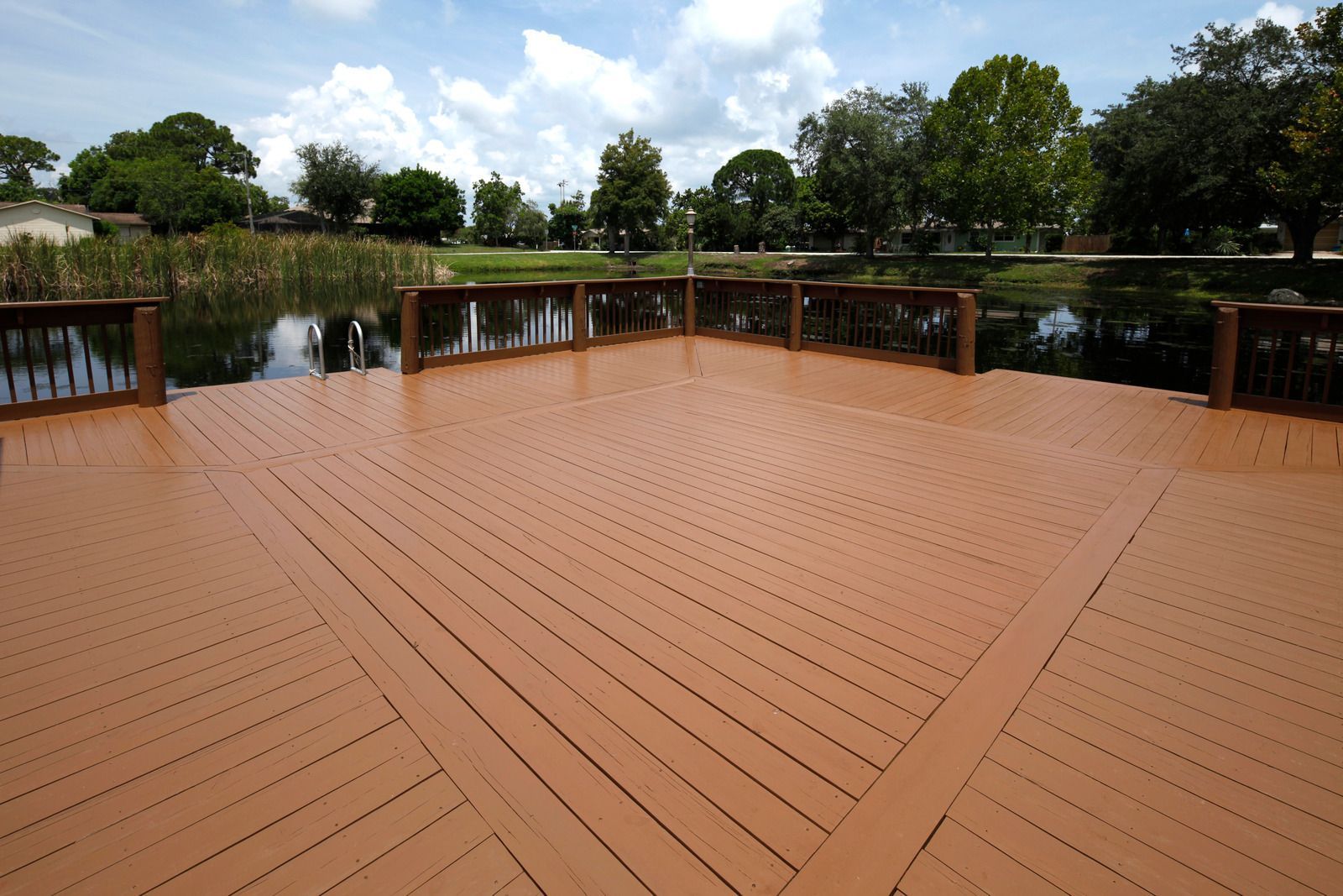 Brown wooden deck overlooking a pond with a cloudy sky and trees in the background.