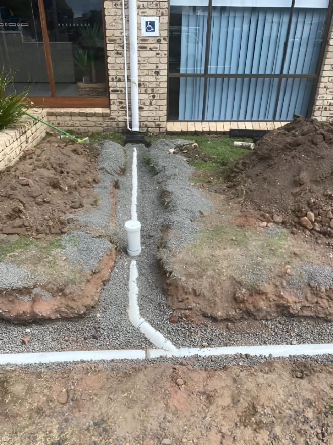 A Drain Pipe Is Being Installed In The Dirt In Front Of A House — Casino Plumbing In Casino, NSW