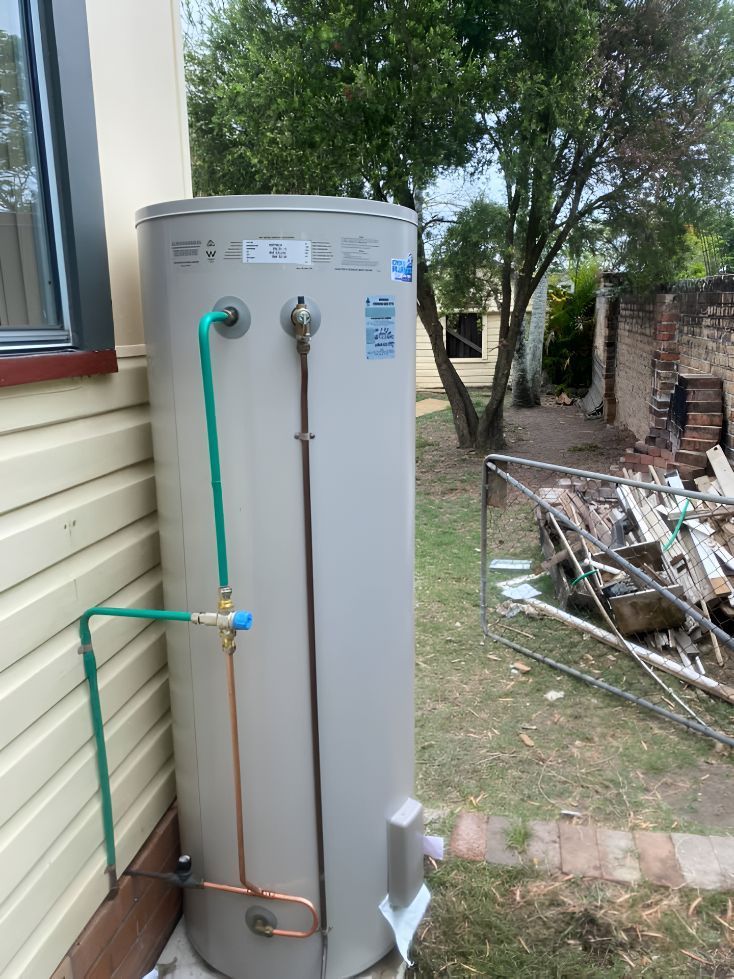 A Water Heater Is Sitting Outside Of A House Next To A Window — Casino Plumbing In Casino, NSW
