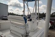 White fishing boat console with twin chairs on a dock, under a canopy, on calm water.