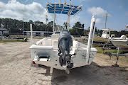 White motorboat on a trailer at a boatyard, with an outboard motor and blue canopy frame.