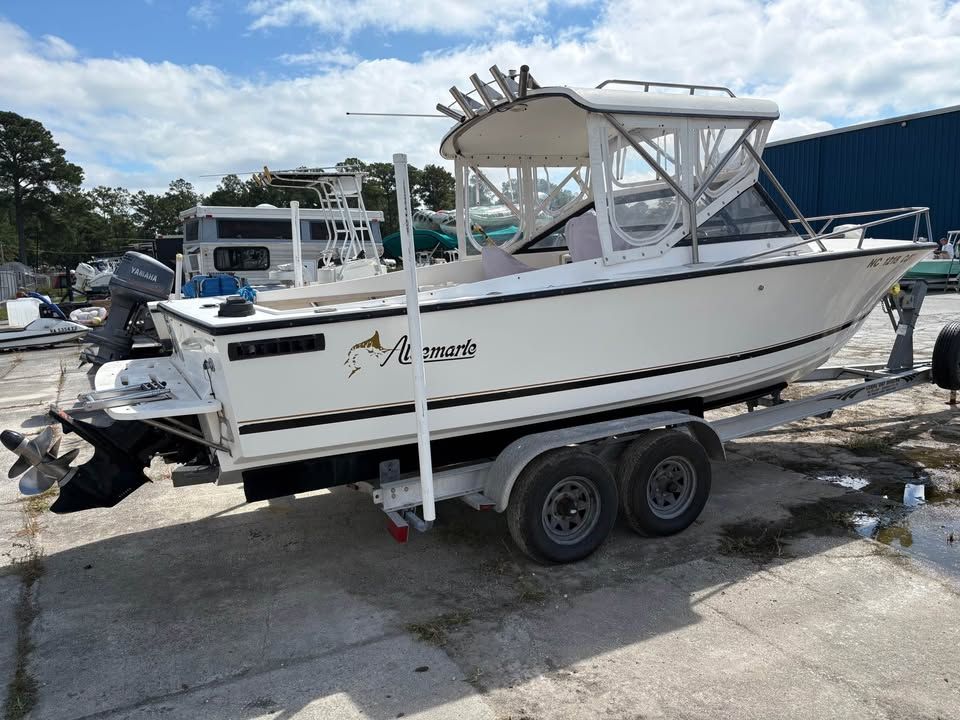 White center-console boat on a trailer in a boatyard, with a canopy and blue building in the background