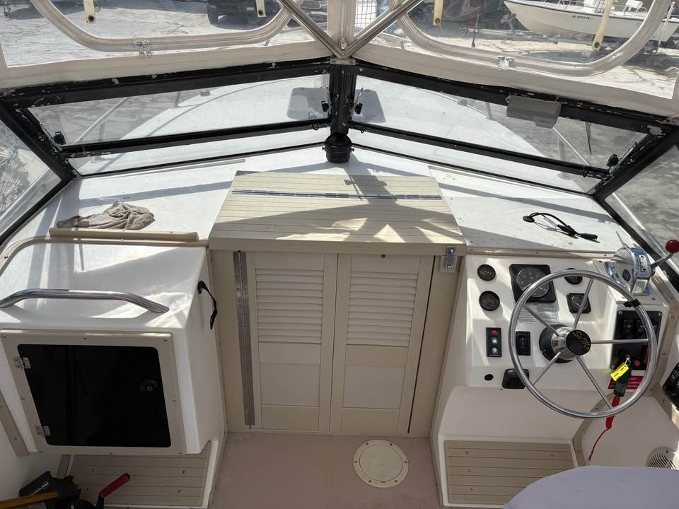 Boat cockpit with white cabinets, tan center hatch, and steering wheel under a clear canopy