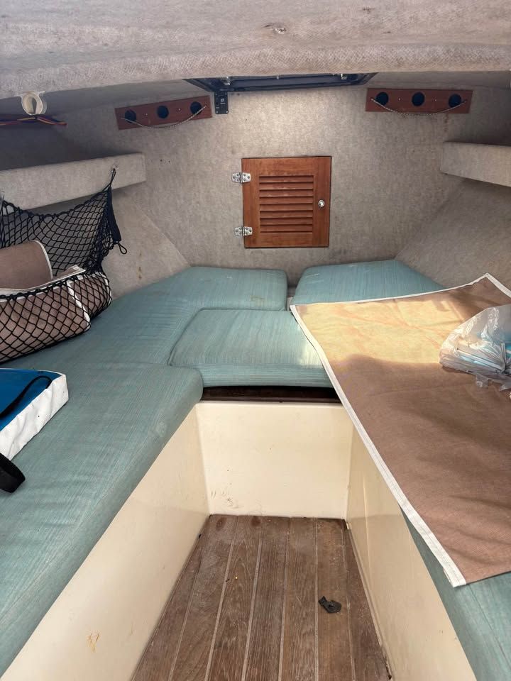 Compact boat cabin with teal bench seating, wood floor, and a small central hatch/door.