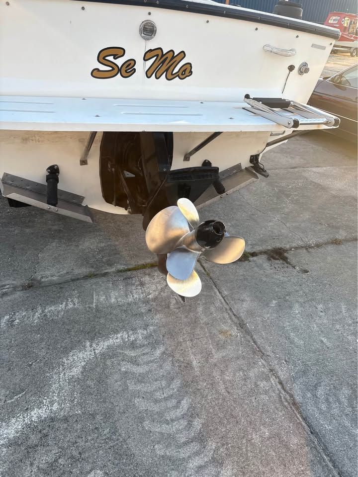 Rear view of a white boat named So Mo with a propeller and stern drive over concrete.