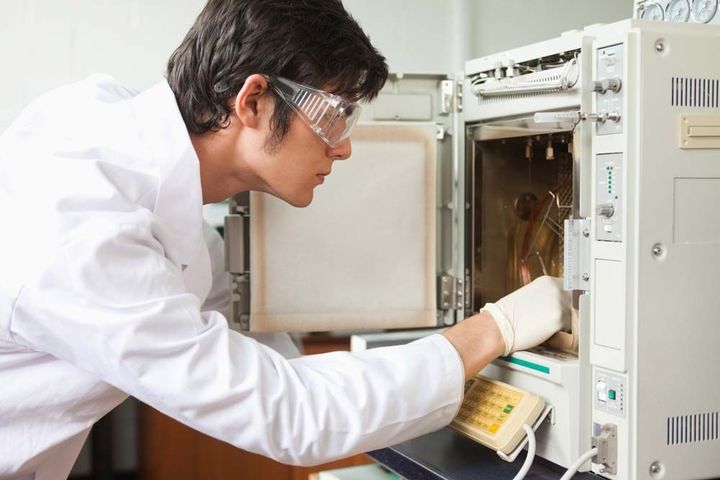A person wearing goggles and white coat looking at an open microwave. A person wearing goggles and white coat looking at an open microwave.