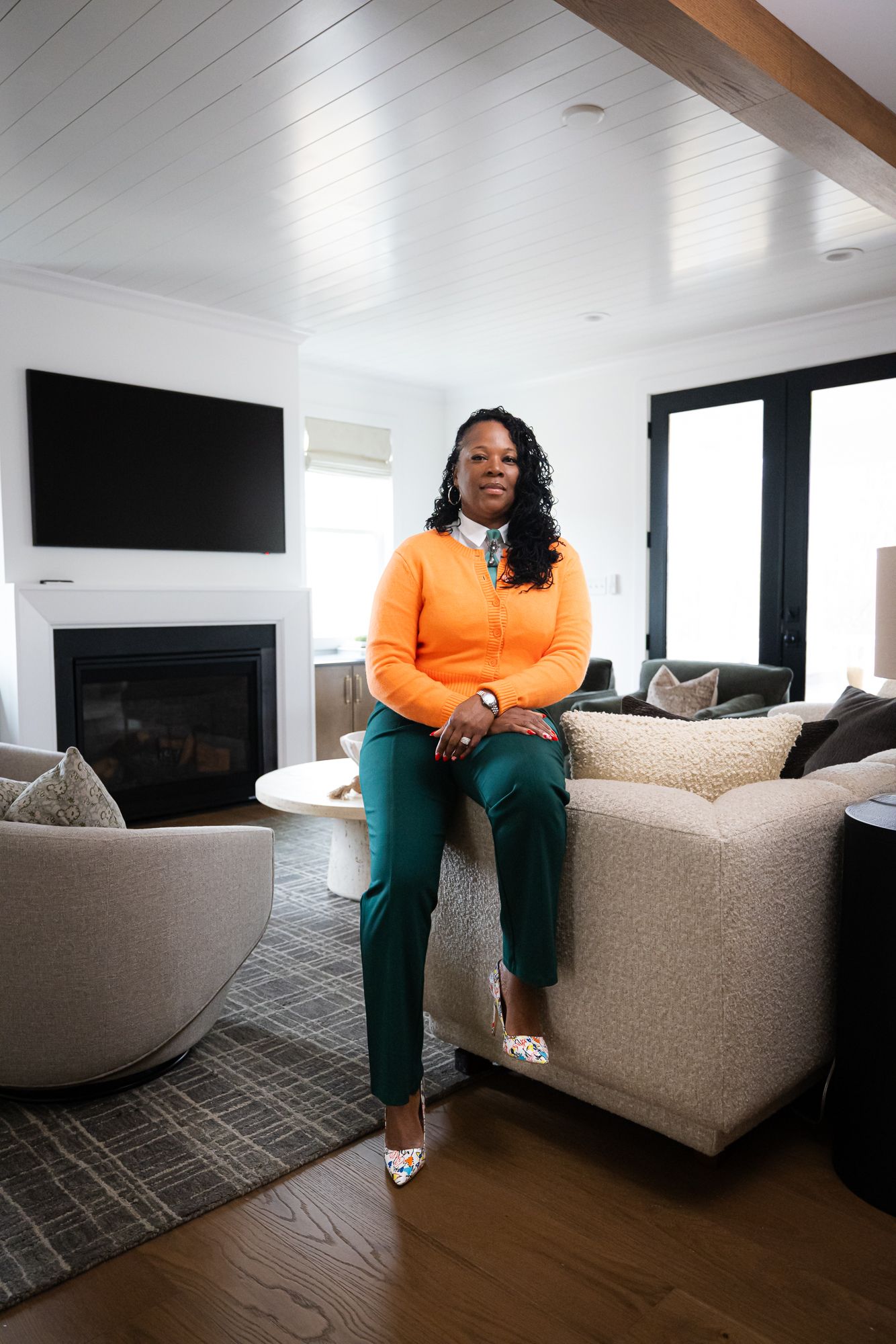 Person seated on a beige couch in a bright living room with a fireplace and wall-mounted TV.
