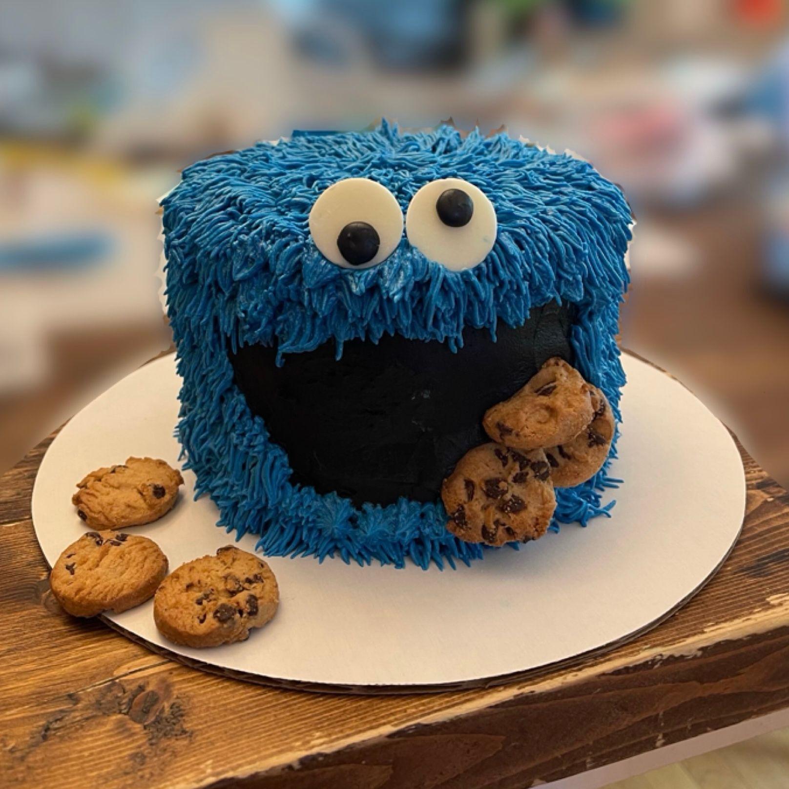 A Cookie Monster-themed birthday cake decorated with blue frosting fur, white googly eyes, and chocolate chip cookies.