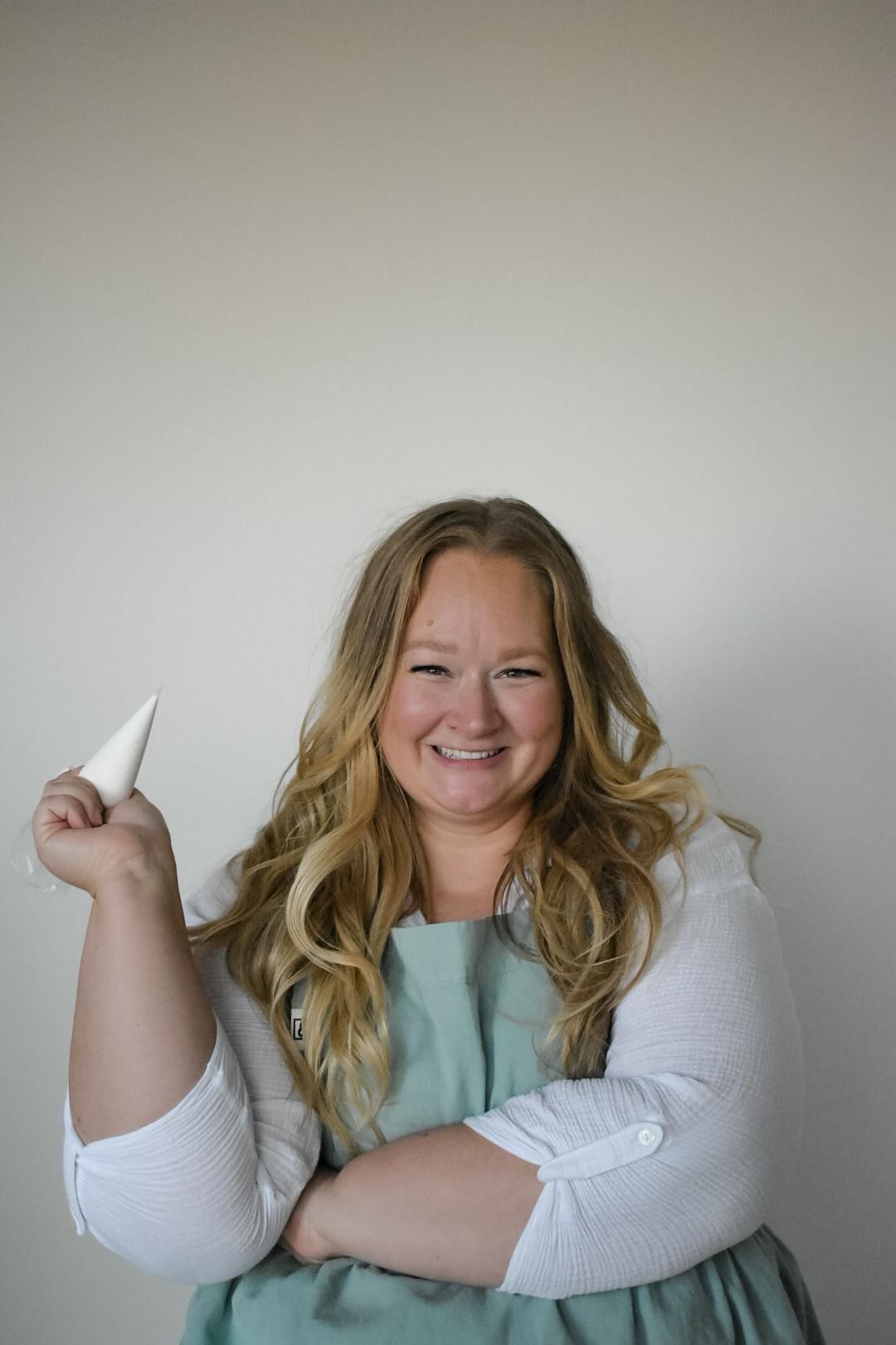 Woman holding pastry cone, smiling, wearing an apron, against a white background.