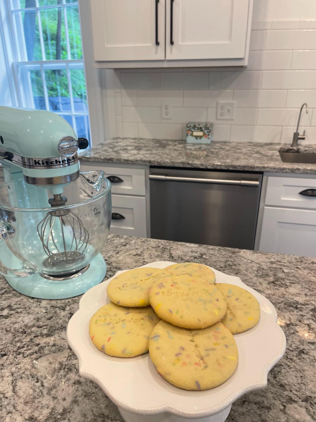 Cookies on a white cake stand in a kitchen with a blue stand mixer.