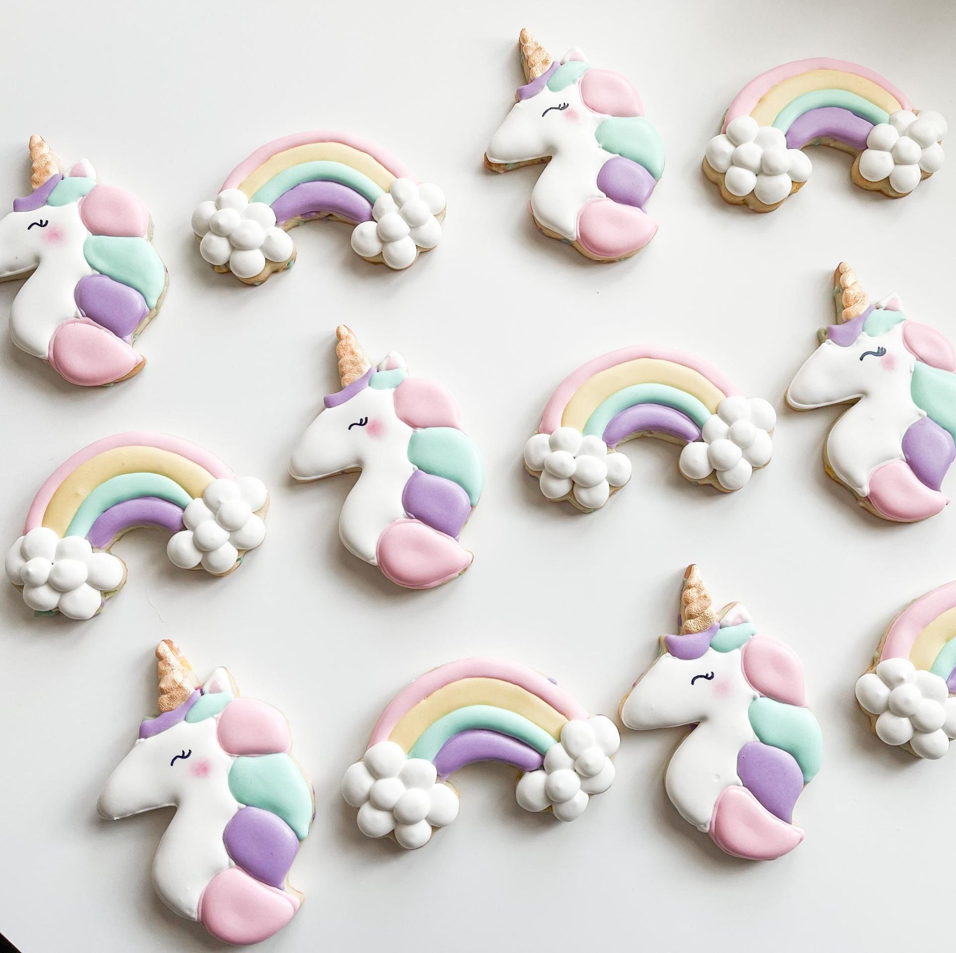 A top-down view of pastel unicorn and rainbow-shaped sugar cookies arranged on a plain white surface.