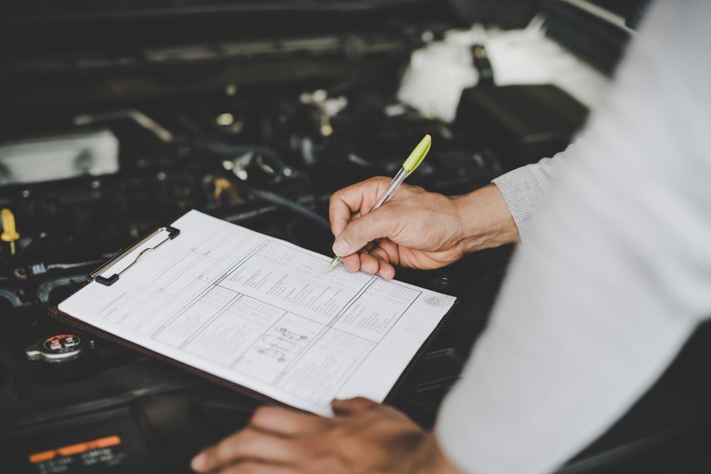 A Man Is Writing on A Clipboard in Front of A Car Engine — Modern Motors-Nabiac in Nabiac, NSW
