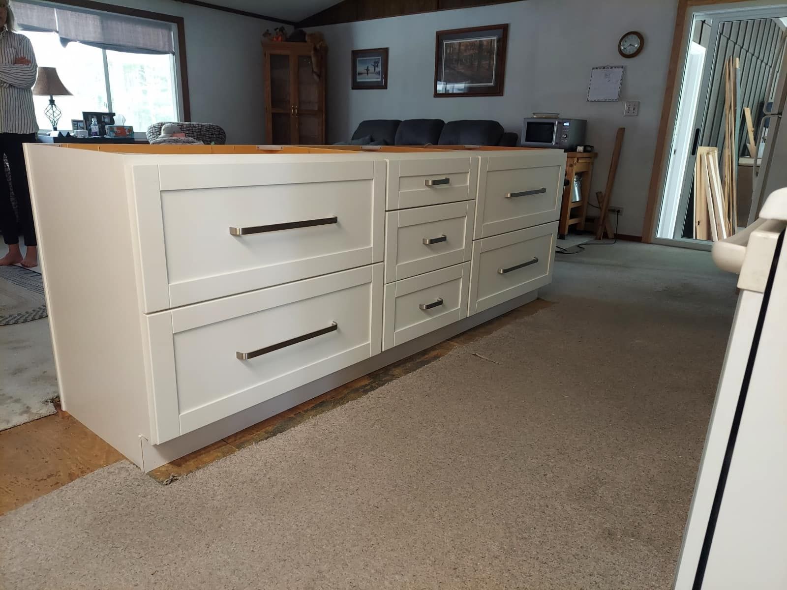 White kitchen island with drawers and a wooden countertop, in a home with carpet.