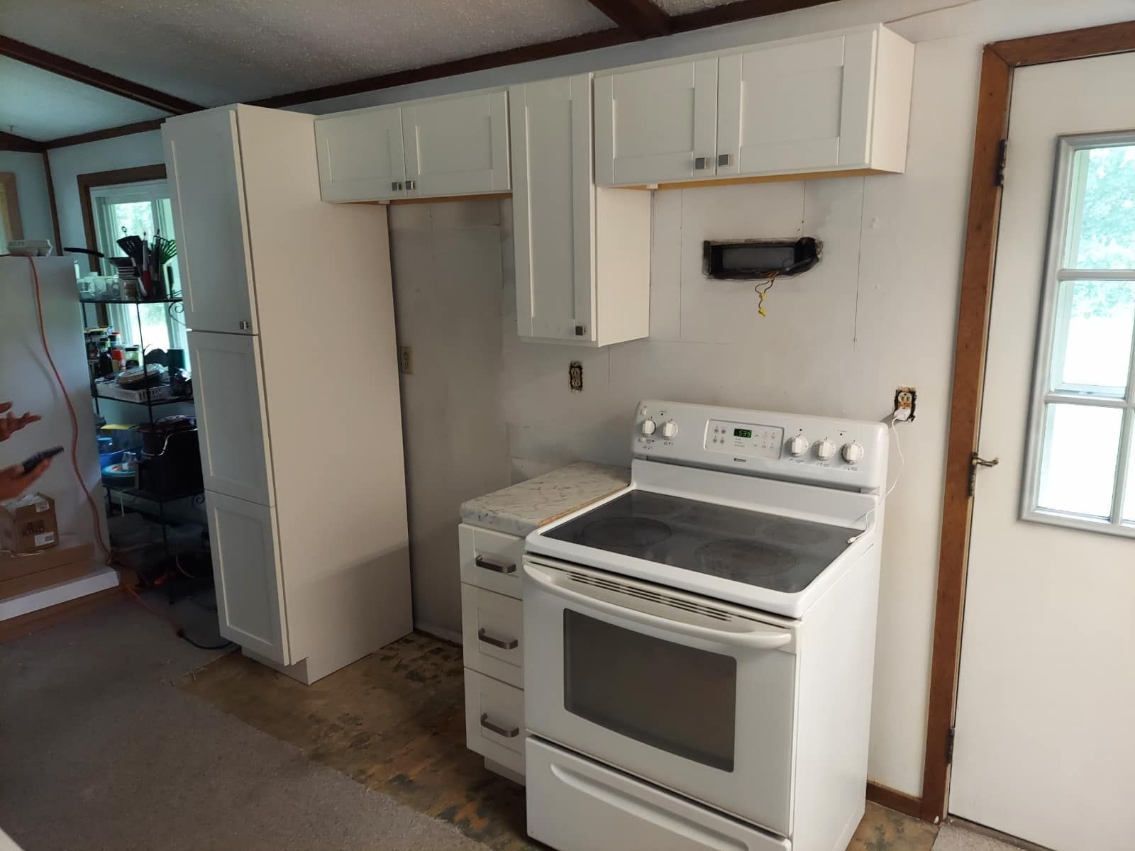 A kitchen with white cabinets and appliances. A stove, refrigerator, and doorway are visible.