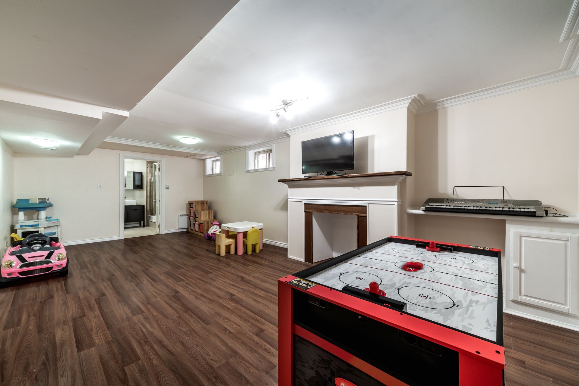 Basement game room with air hockey, TV, toys, and wood-look flooring.