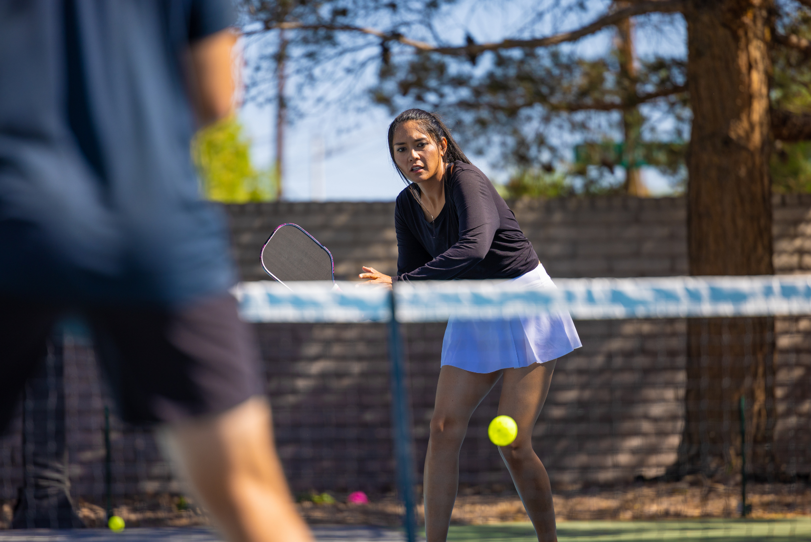 Tennis player in black top and light blue skirt hits a ball on an outdoor court.