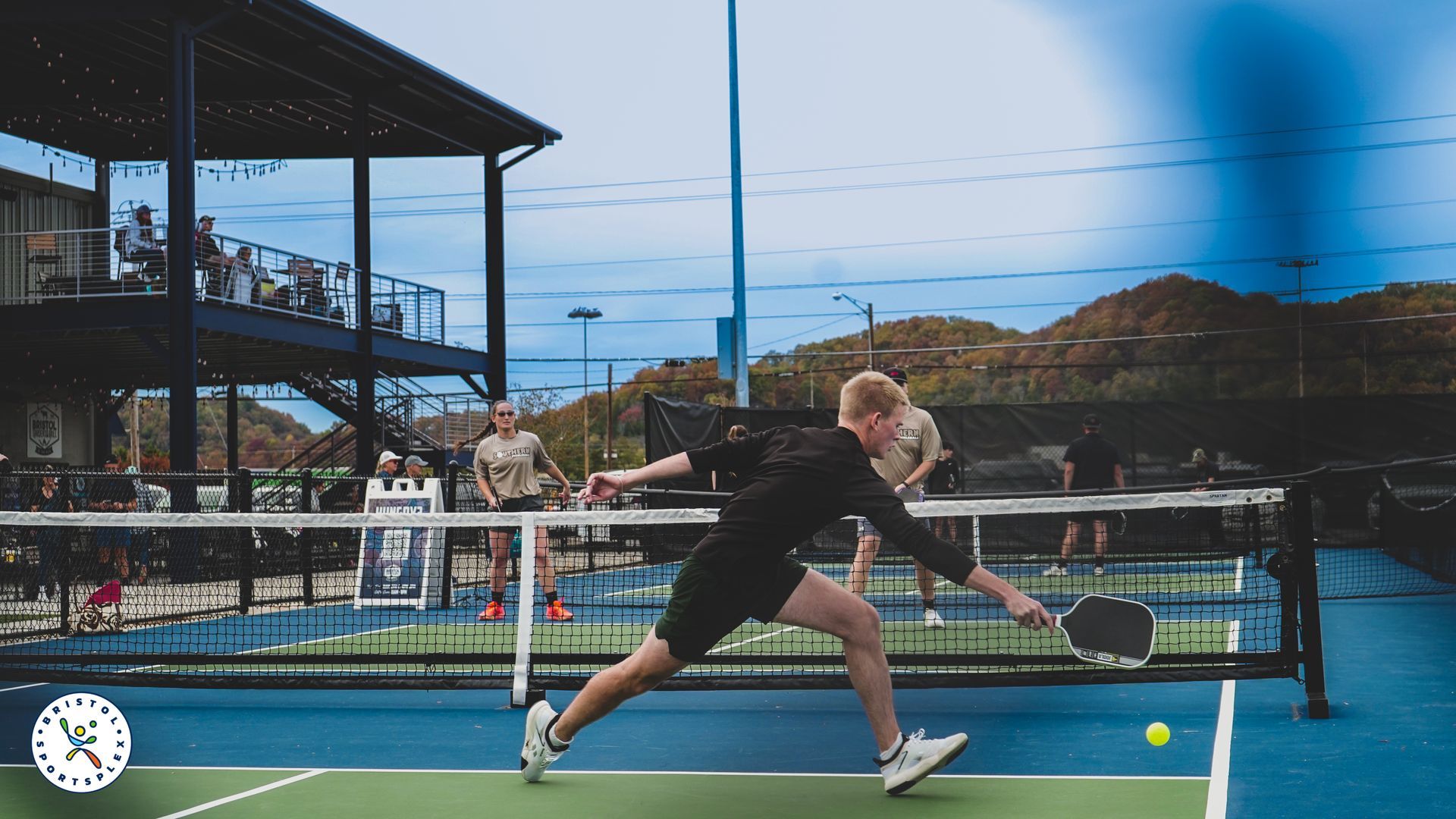 Padel player in neon pink and teal gear ready at the net on an outdoor court