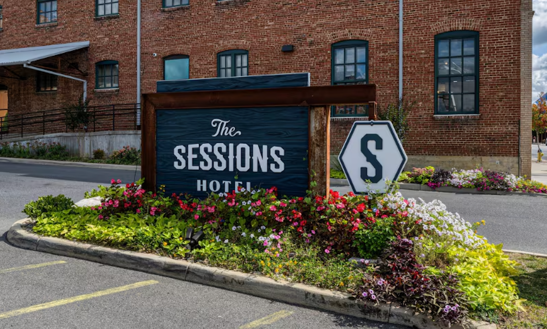 The Sessions Hotel sign in a landscaped flower bed outside a brick building.