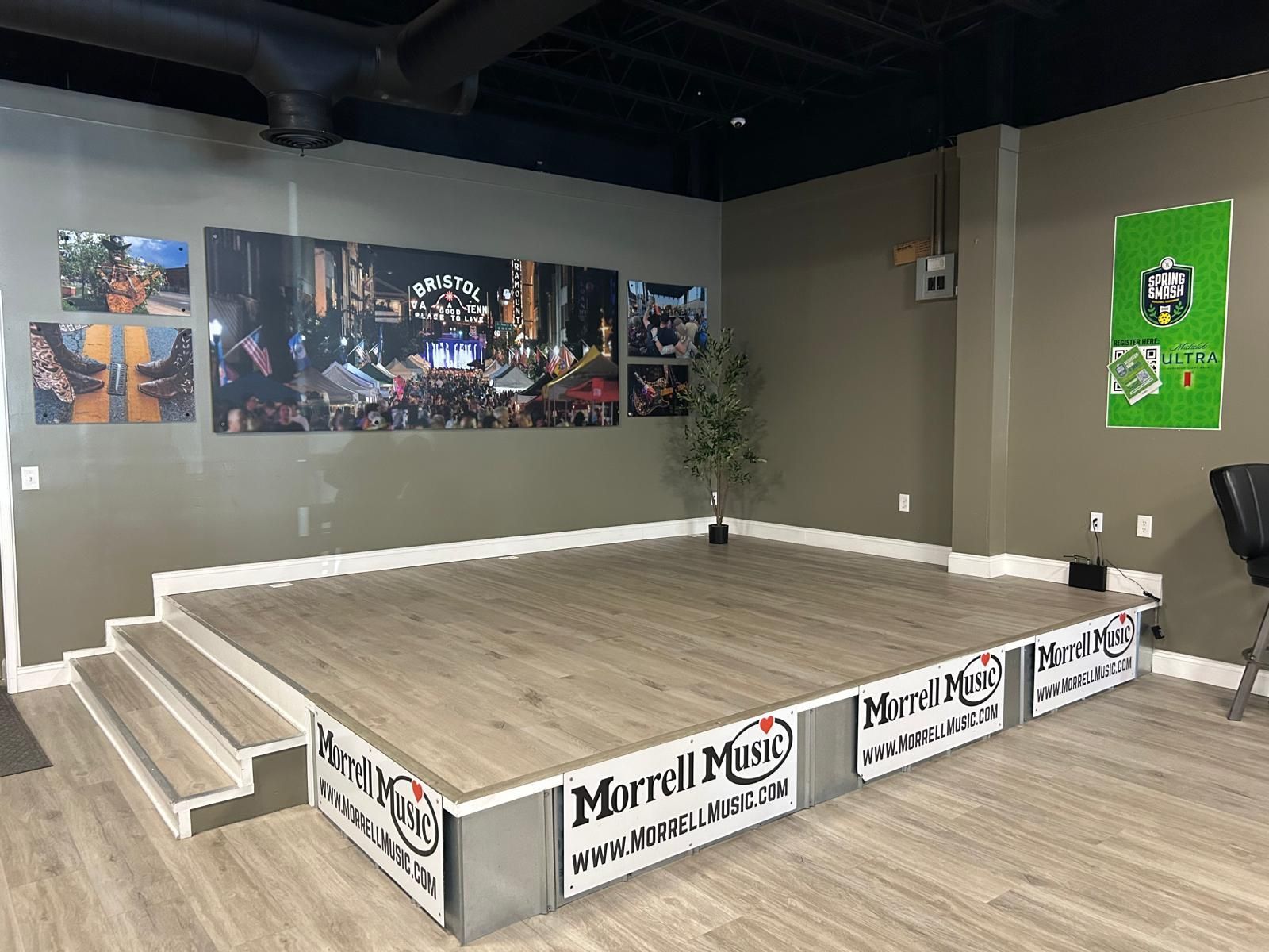Small indoor stage with white steps, wood floor, city mural, and posters on gray walls