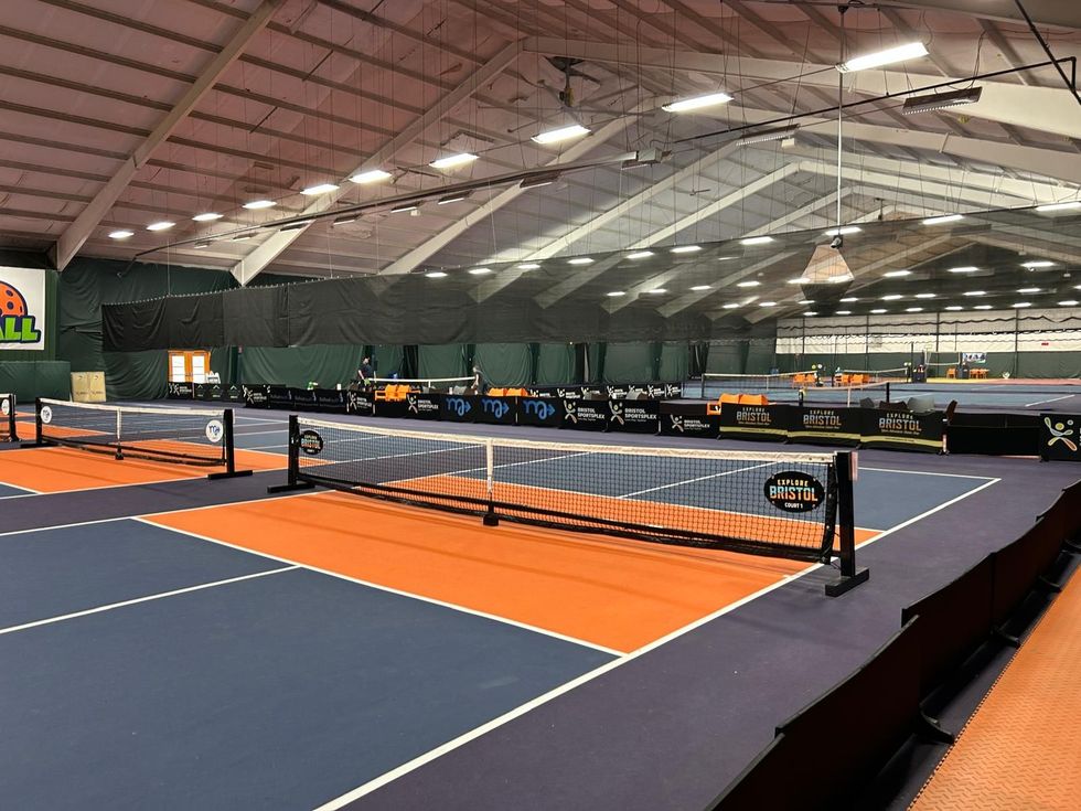 Indoor pickleball courts with blue and orange flooring under a large arched roof