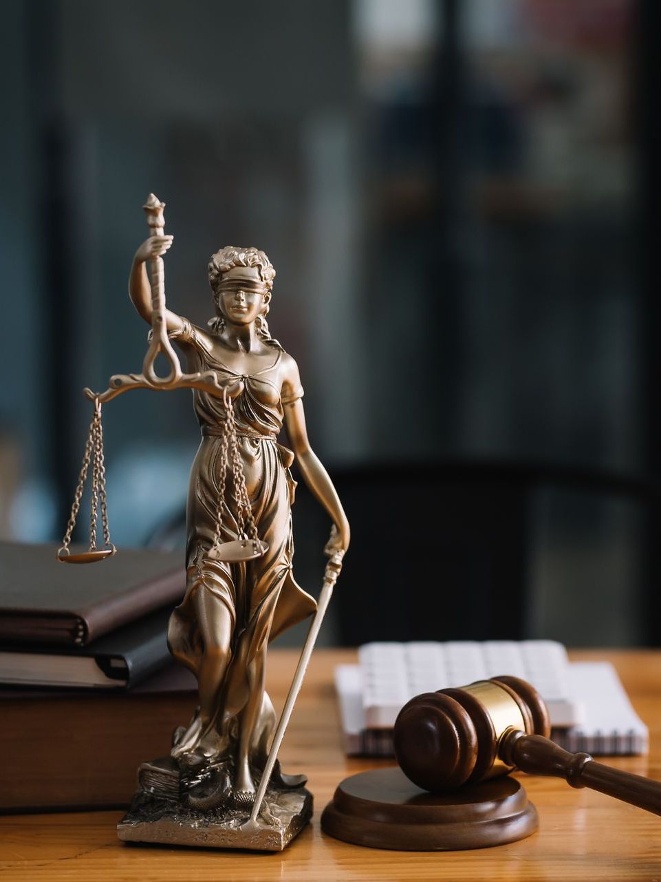 A statue of justice is sitting on a wooden table next to a gavel.