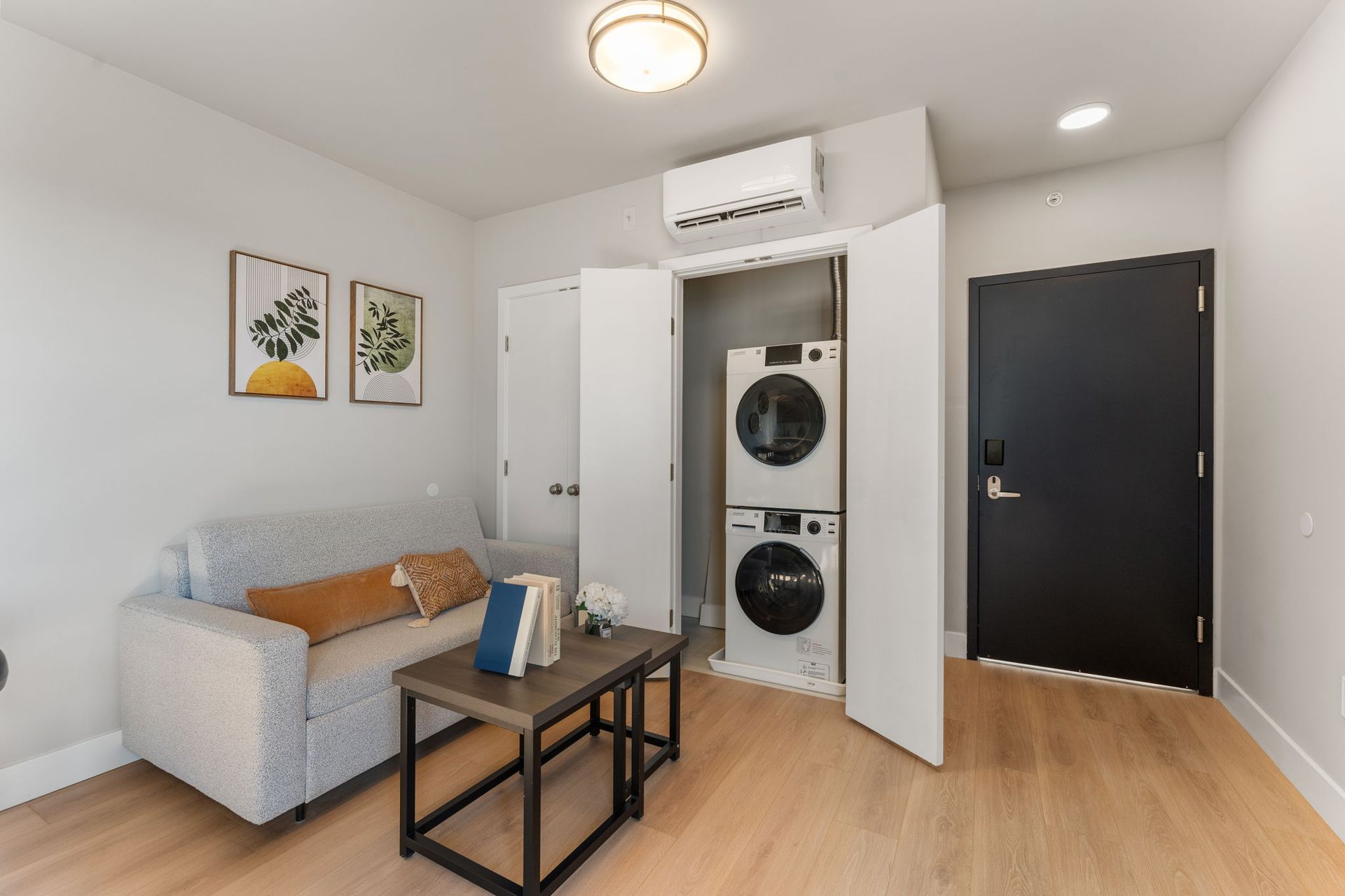 A living room with a couch , coffee table , and washer and dryer stacked on top of each other.