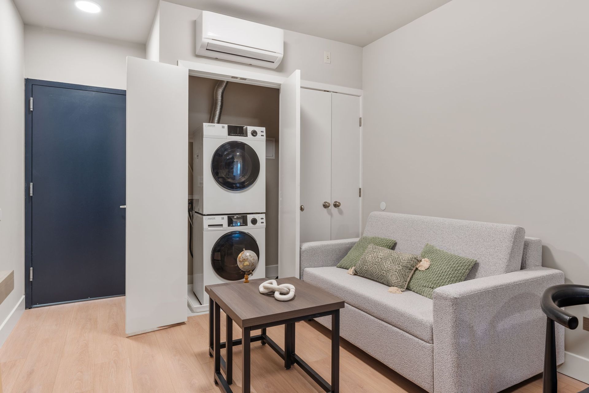 A living room with a couch and a washer and dryer stacked on top of each other.