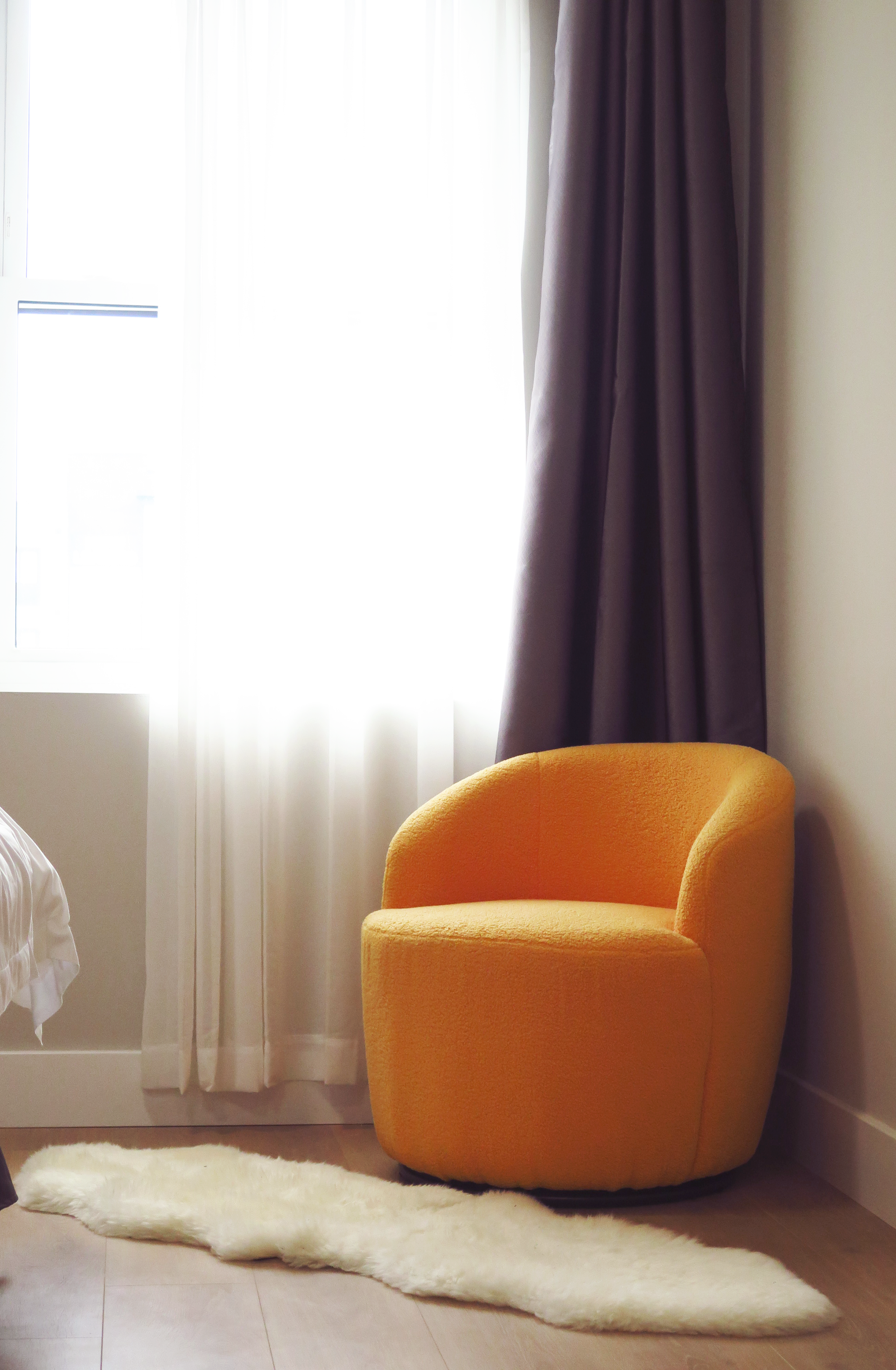 A yellow chair is sitting in front of a window in a bedroom.