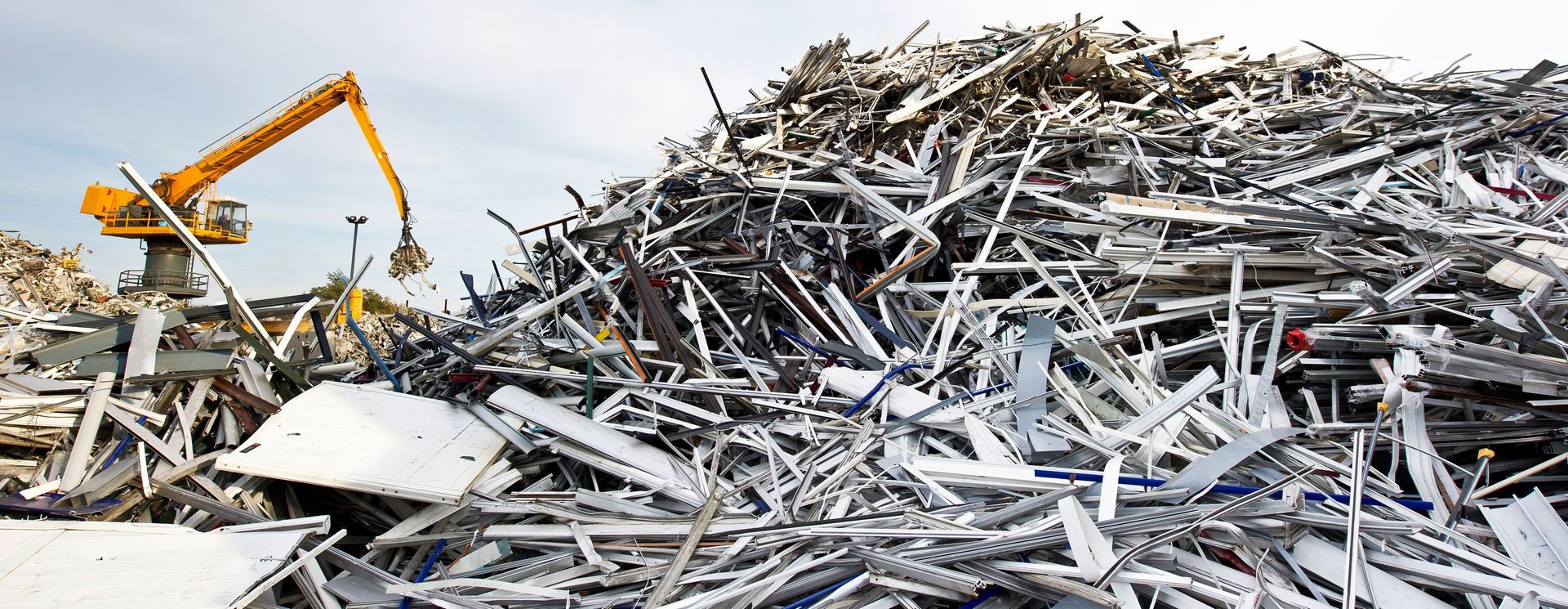 Large stack of aluminum and ferrous materials scrap with yellow crane in the background. Large stack of aluminum and ferrous materials scrap with yellow crane in the background.