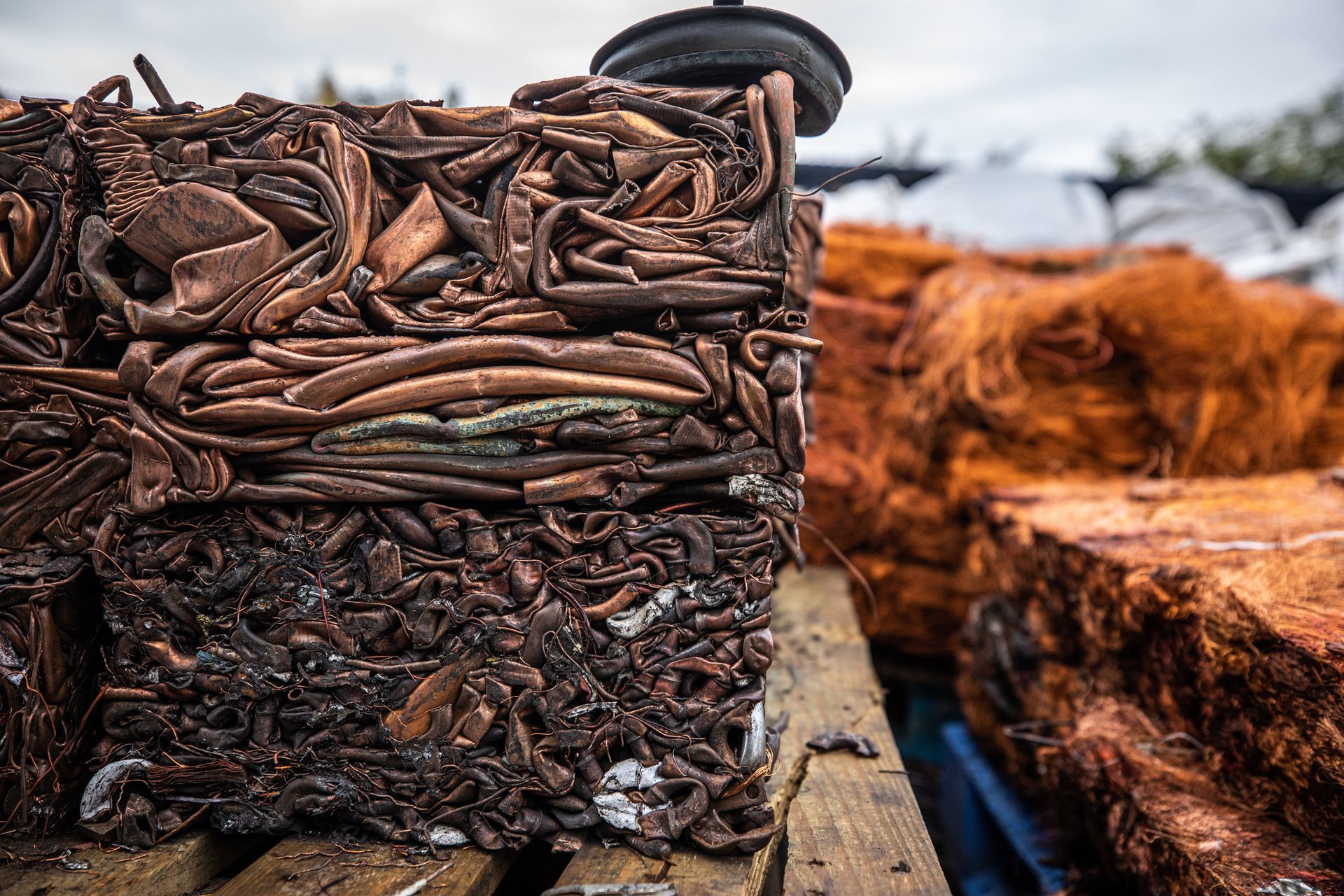 Compressed copper scrap bales, pressed into square shapes, sitting on a wooden pallet.