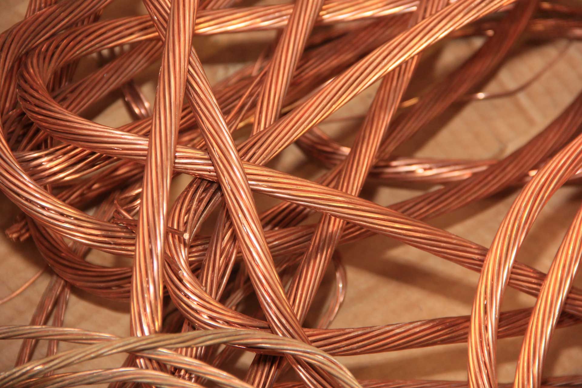 Tightly coiled copper wires with a shiny metallic surface. Close-up of a tangled pile of copper electrical wires, showing their twisted strands and reddish-brown color.