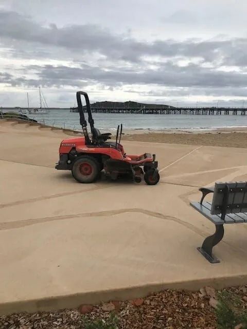 A Red Lawn Mower Is Parked On The Sidewalk Near The Beach — Michael Flick Horticulture in Coffs Harbour, NSW